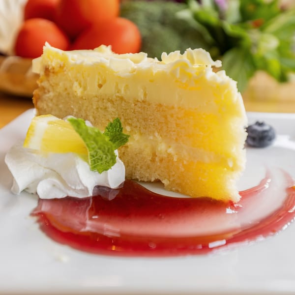 Slice of lemon cake with whipped cream, mint, and berry sauce on a white plate.