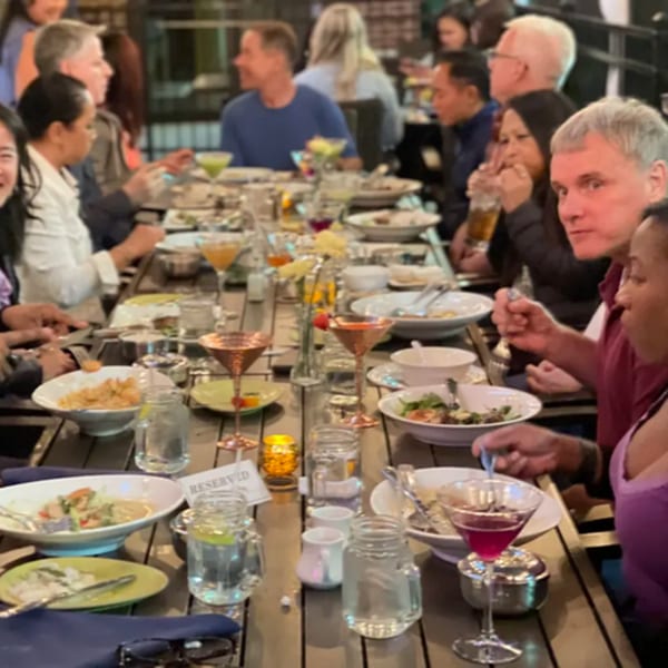 Diners enjoying Thai cuisine and drinks at a long communal table in Colonial Kitchen and Bar.
