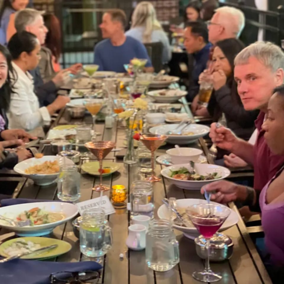 Diners enjoying Thai cuisine and drinks at a long communal table in Colonial Kitchen and Bar.