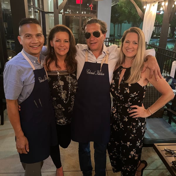 Four smiling people, two wearing Colonial Kitchen aprons, pose together on a restaurant patio at night.