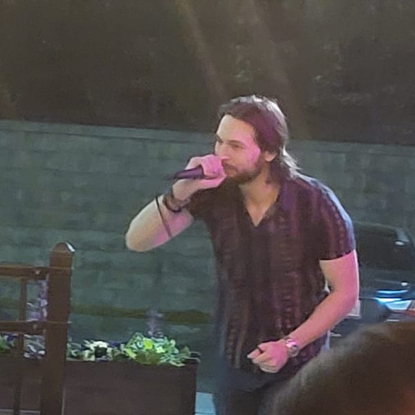 A man with long hair and a beard sings into a microphone at Colonial Kitchen and Bar.