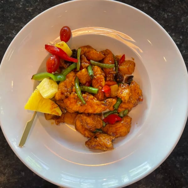 Sweet and sour chicken with pineapple, bell peppers, green beans, and cherry tomatoes on a white plate.