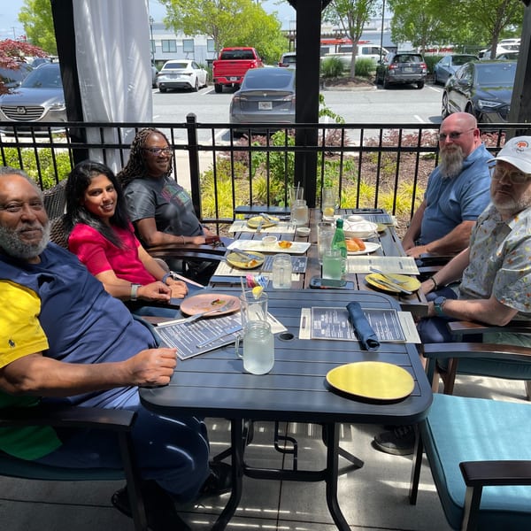 Five people smiling and dining at an outdoor table at Colonial Kitchen and Bar Thai Restaurant.