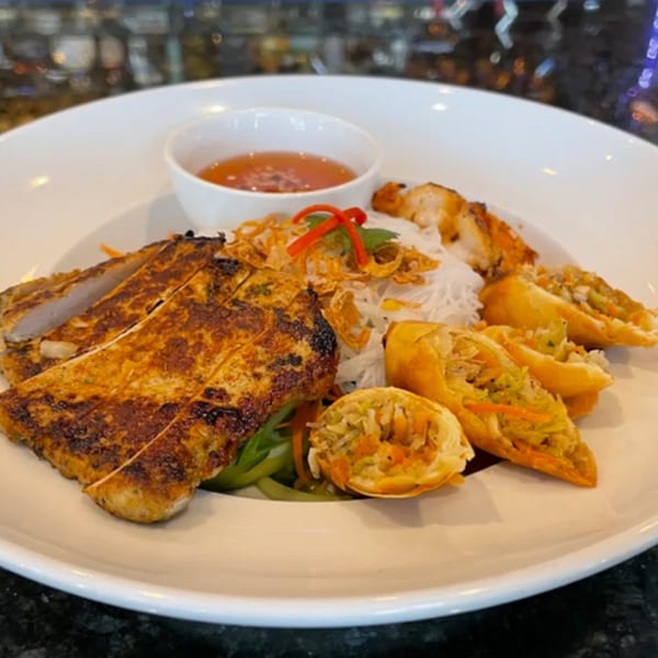 Grilled chicken, spring rolls, vermicelli noodles, and a dipping sauce on a white plate.