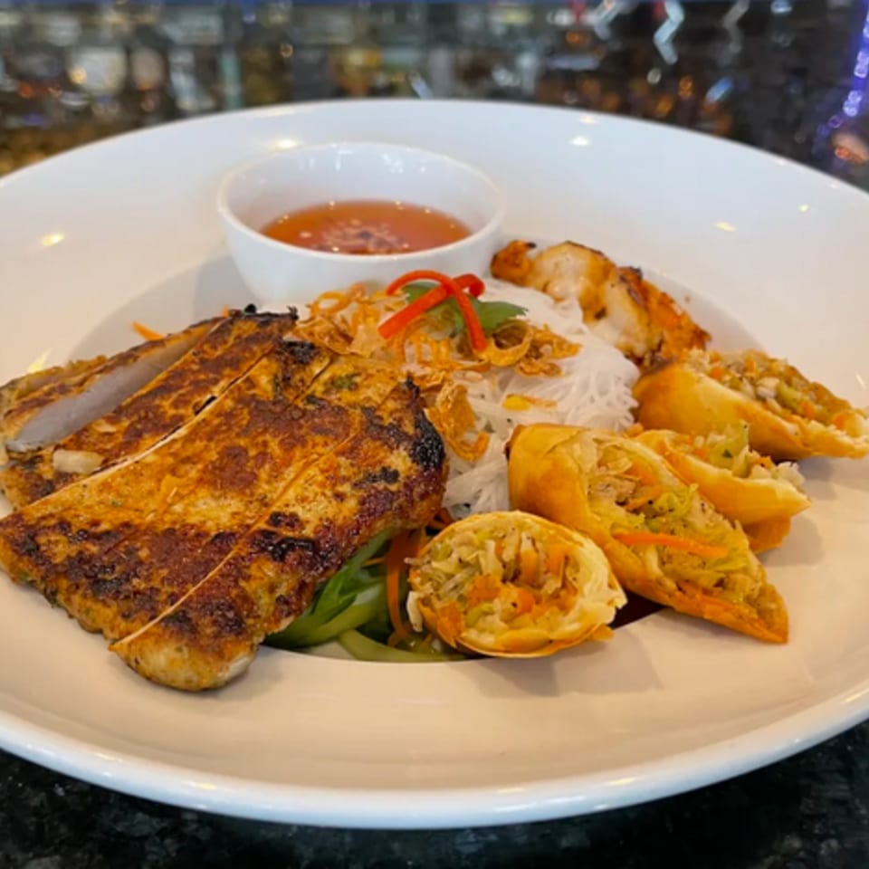 Grilled chicken, spring rolls, vermicelli noodles, and a dipping sauce on a white plate.