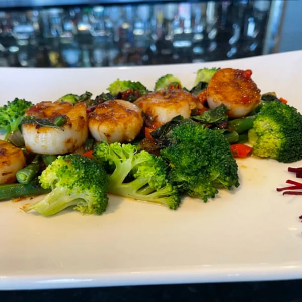 Pan-seared scallops with broccoli and green beans on a white rectangular plate.