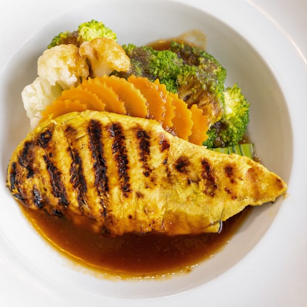 Grilled chicken breast with broccoli, cauliflower, and carved carrots in a rich sauce.