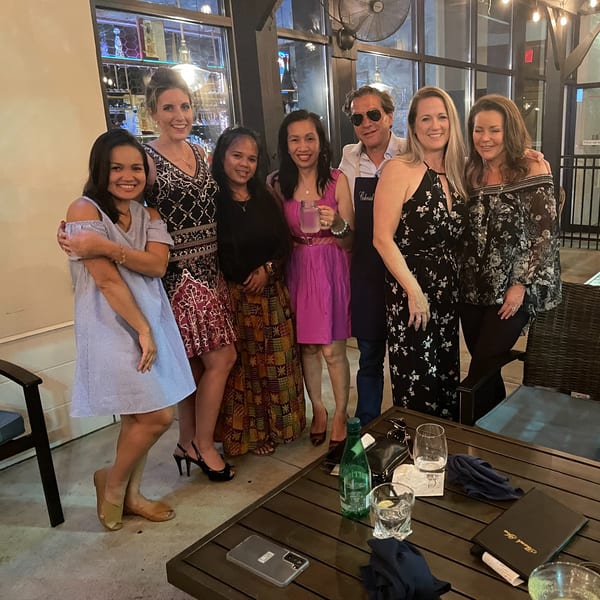 Seven smiling people, including a man in sunglasses, pose together at Colonial Kitchen and Bar.