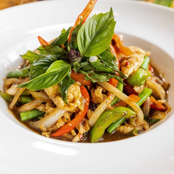 Close-up of a Thai stir-fry with chicken, green beans, bell peppers, onions, and basil.