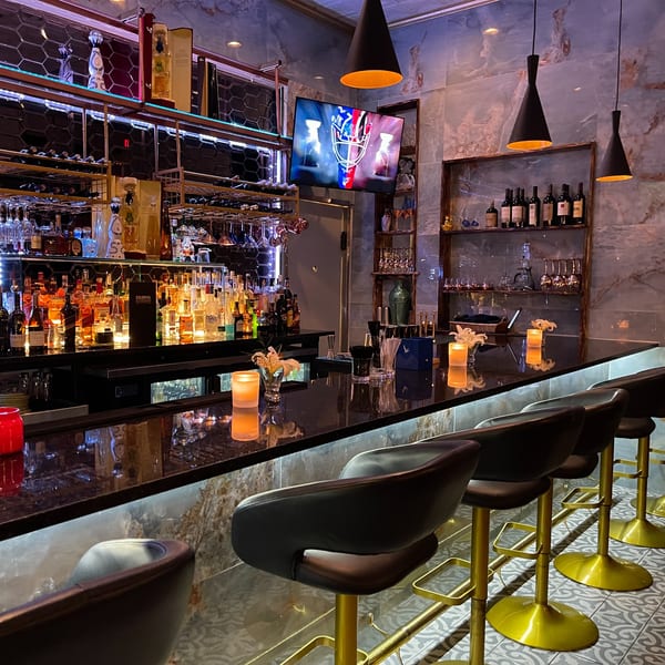 The Colonial Kitchen and Bar features a well-stocked bar with bottles, glasses, and modern lighting.