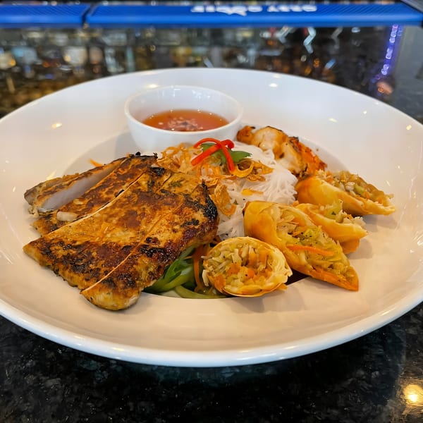 Grilled chicken, spring rolls, rice noodles, and a dipping sauce on a white plate.