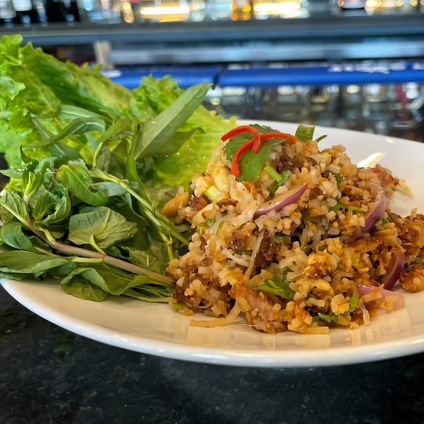 Thai crispy rice salad with red onions, herbs, and lettuce on a white plate.