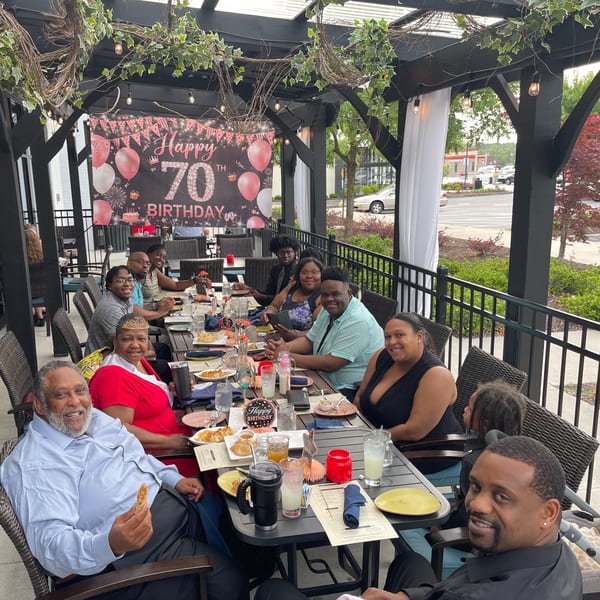 A large group of people celebrating a 70th birthday on an outdoor patio at Colonial Kitchen and Bar.