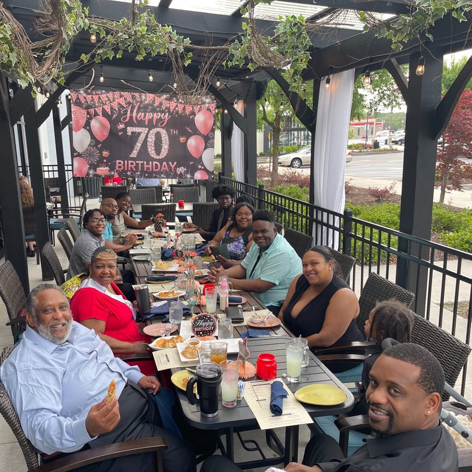 A large group of people celebrating a 70th birthday on an outdoor patio at Colonial Kitchen and Bar.